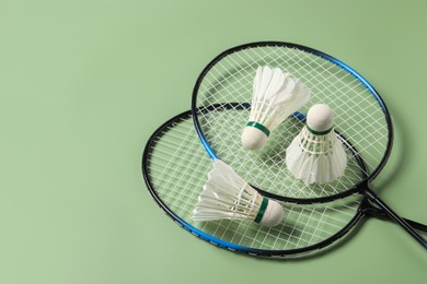 Photo of Feather badminton shuttlecocks and rackets on green background, above view. Space for text