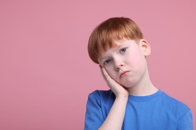 Portrait of sad little boy on pink background, space for text