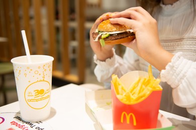 Photo of WARSAW, POLAND - SEPTEMBER 04, 2022: Woman with McDonald's burger, French fries and drink at table in cafe, closeup