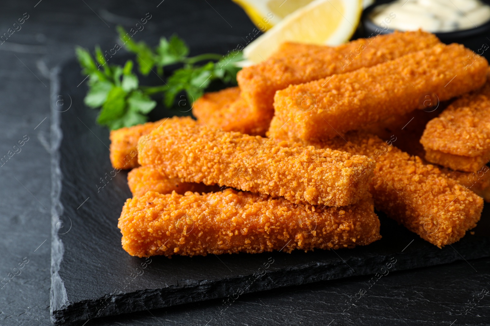 Photo of Fresh breaded fish fingers served on black table, closeup