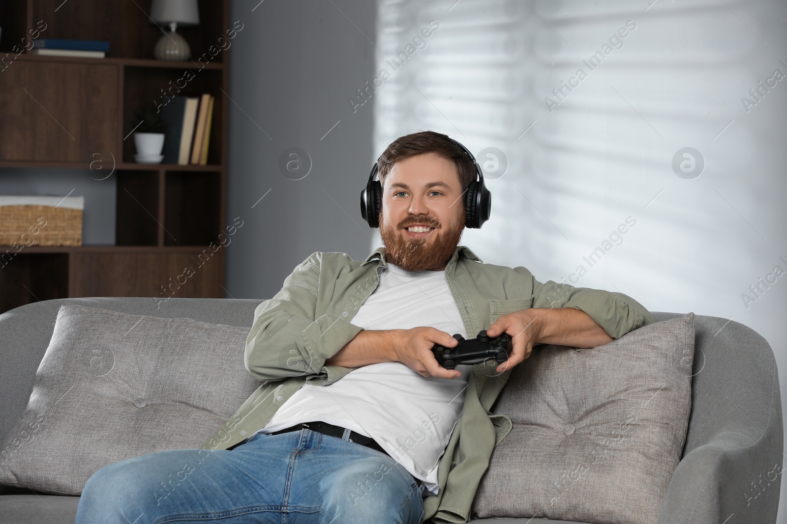 Photo of Happy man in headphones playing video game with controller at home