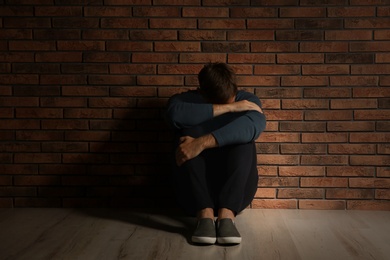 Depressed young man sitting on floor near brick wall