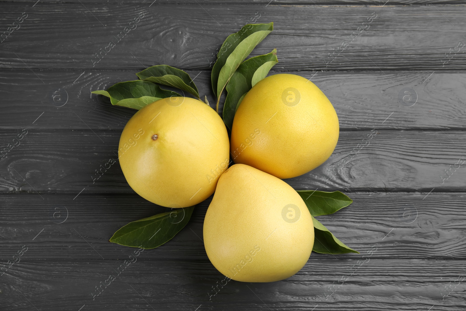 Photo of Fresh whole pomelo fruits and green leaves on grey wooden table, flat lay