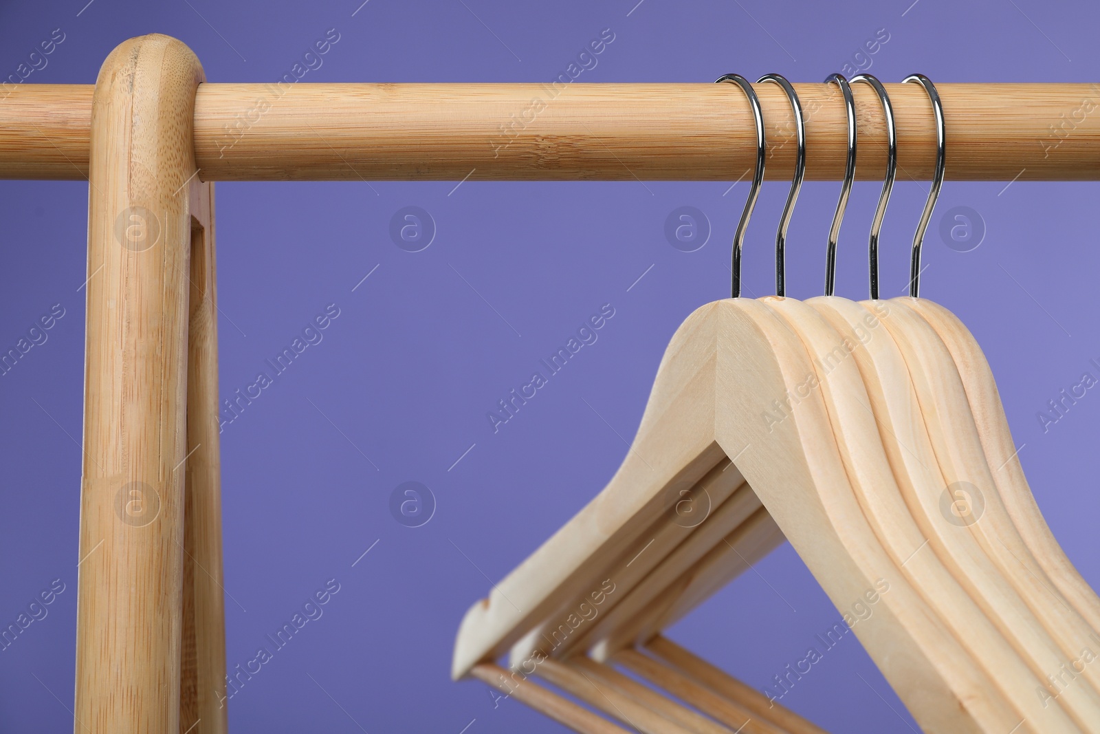 Photo of Empty clothes hangers on wooden rack against purple background, closeup