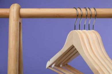 Photo of Empty clothes hangers on wooden rack against purple background, closeup