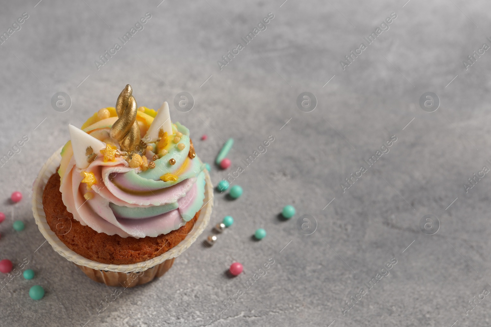 Photo of Cute sweet unicorn cupcake on light grey table, space for text