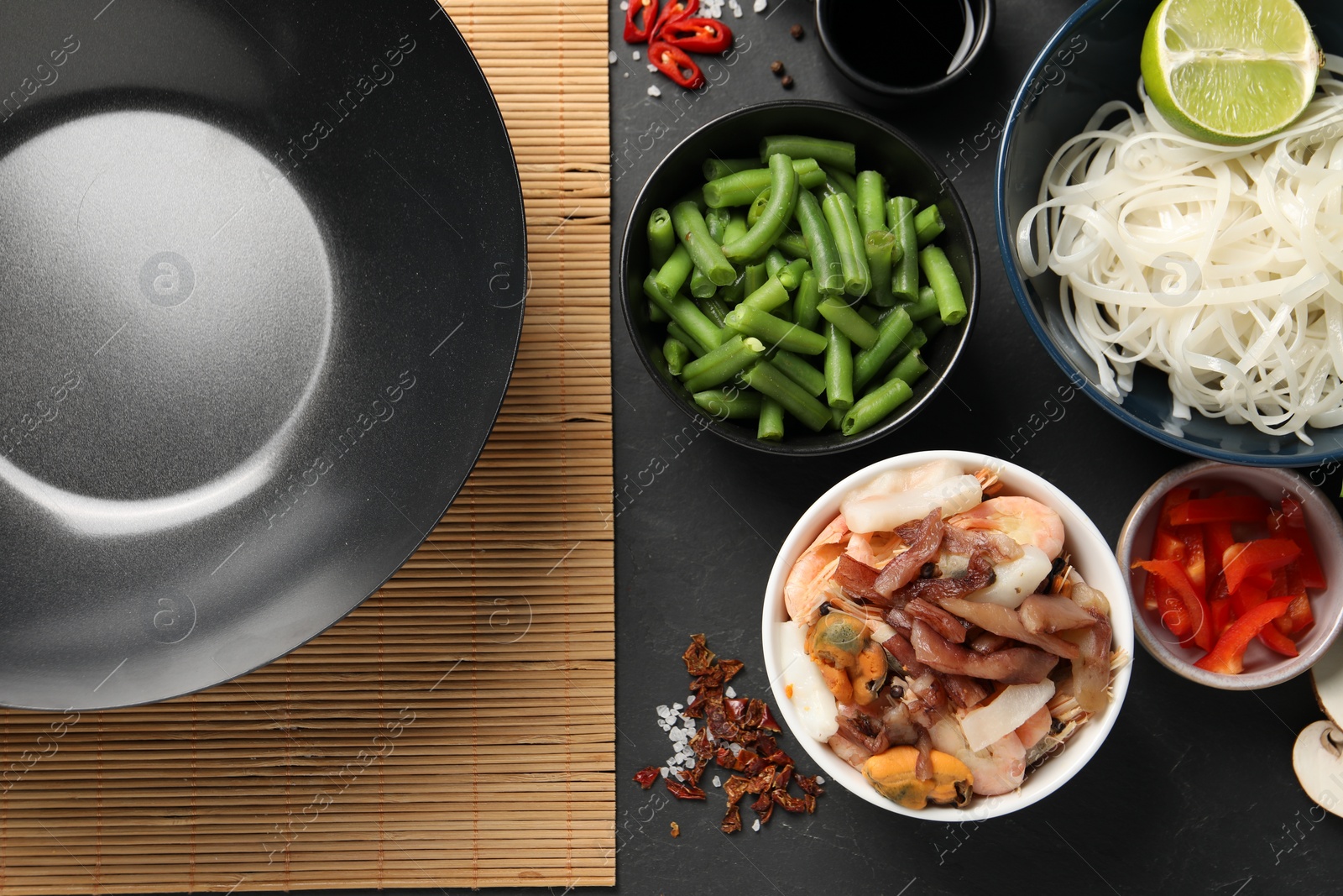 Photo of Flat lay composition with black wok, spices and products on dark textured table