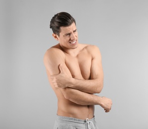 Young man suffering from pain in arm on grey background