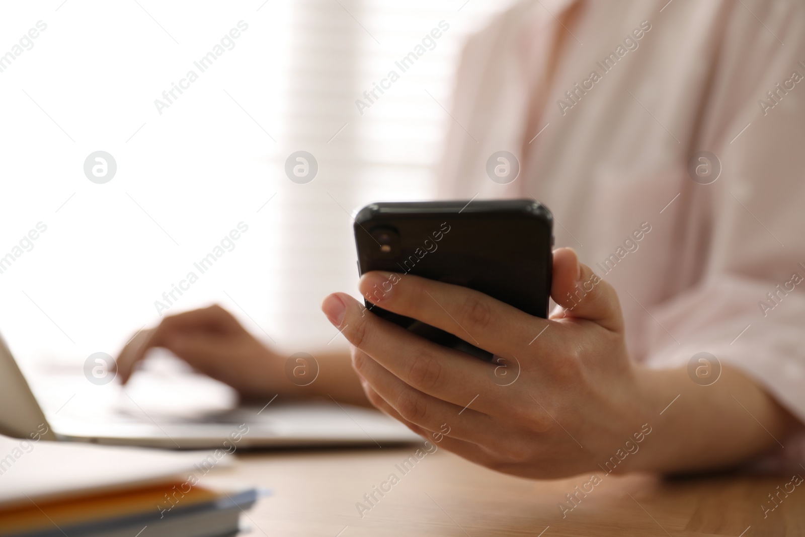 Photo of Woman with smartphone and laptop at table indoors, closeup