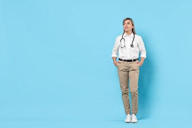 Portrait of happy doctor with stethoscope on light blue background, space for text