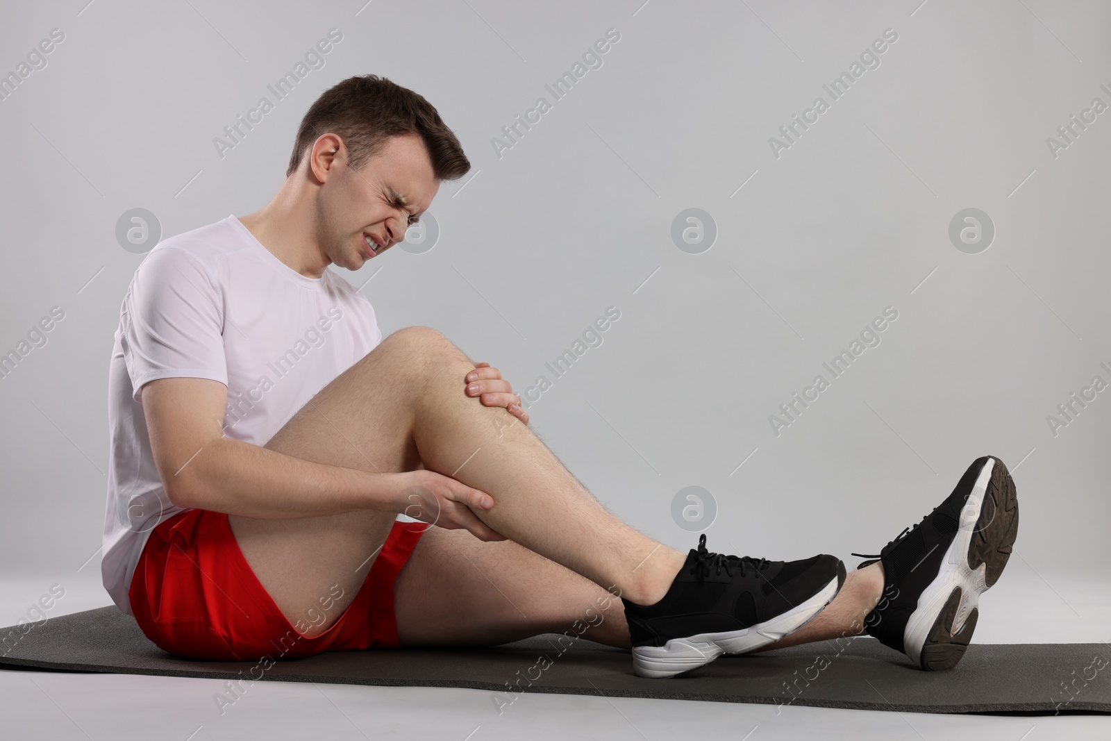 Photo of Man suffering from leg pain on mat against grey background