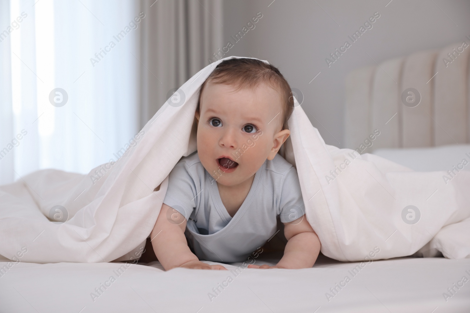 Photo of Cute little baby under soft blanket on bed at home