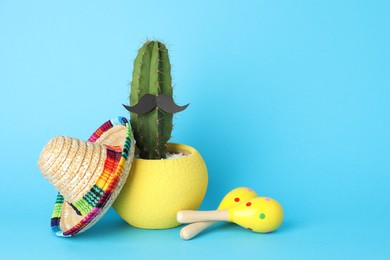 Photo of Mexican sombrero hat, cactus with fake mustache and maracas on light blue background, space for text