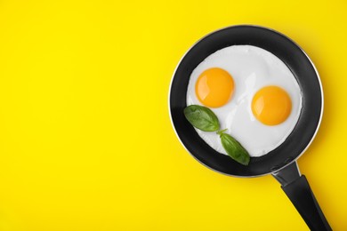 Tasty fried eggs with basil in pan on yellow background, top view. Space for text