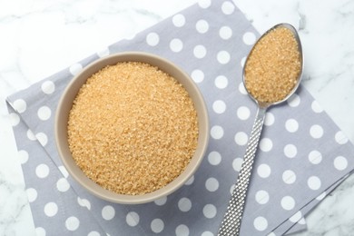 Photo of Brown sugar in bowl and spoon on white marble table, top view