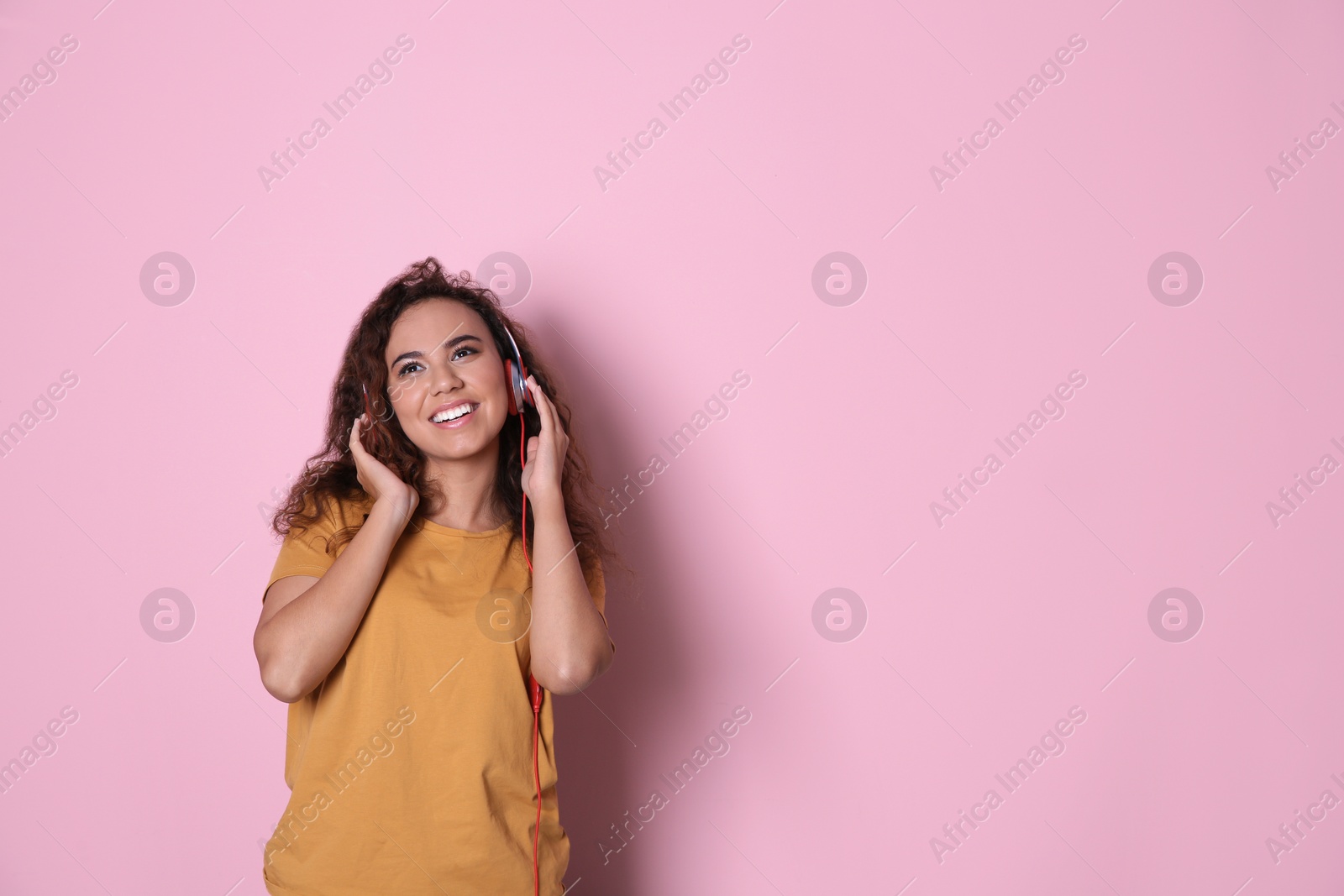 Photo of African-American girl listening to music with headphones on color background, space for text