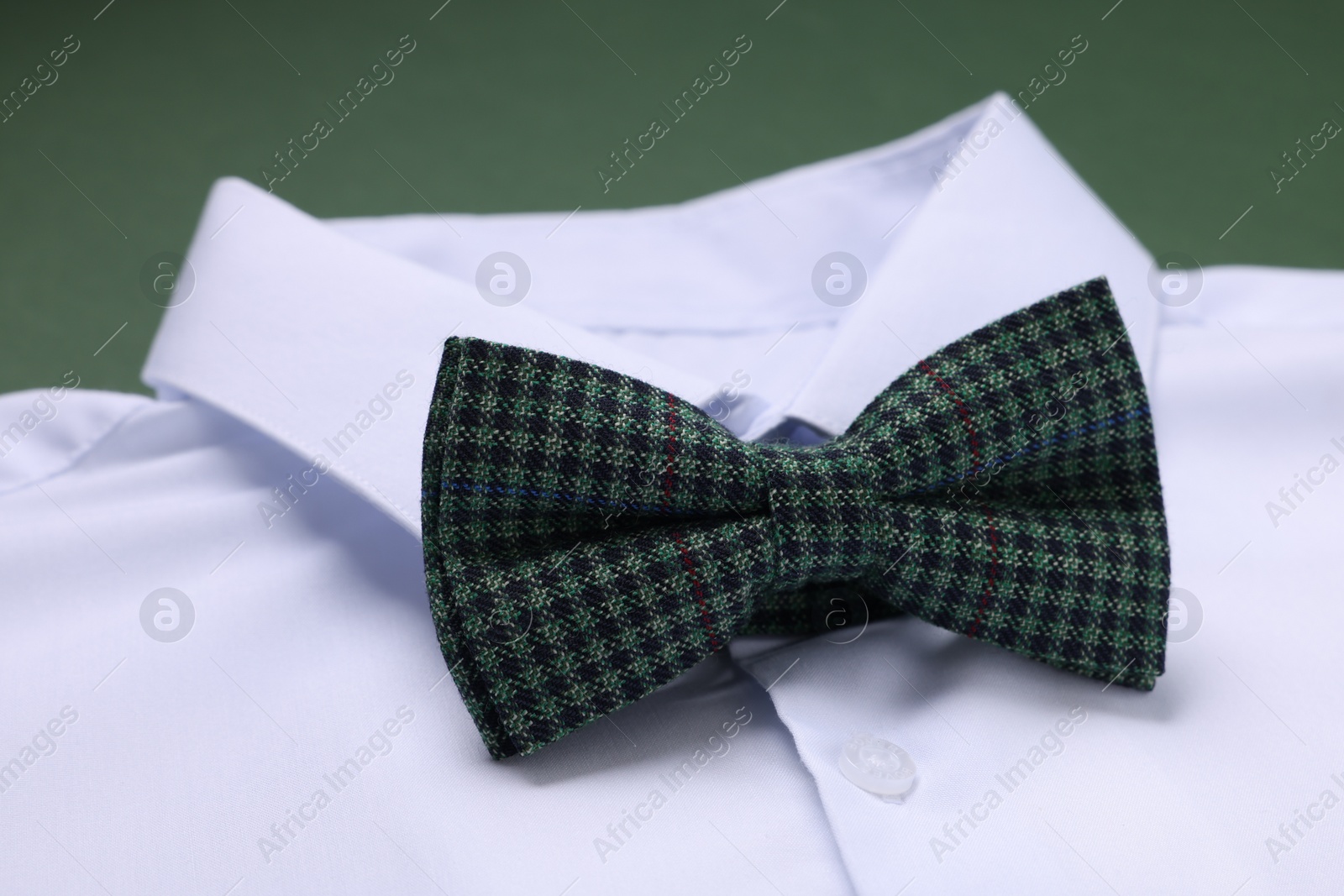 Photo of White shirt with stylish checkered bow tie on green background, closeup