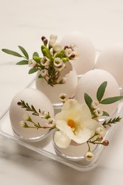 Photo of Easter eggs and beautiful flowers on white marble table, closeup