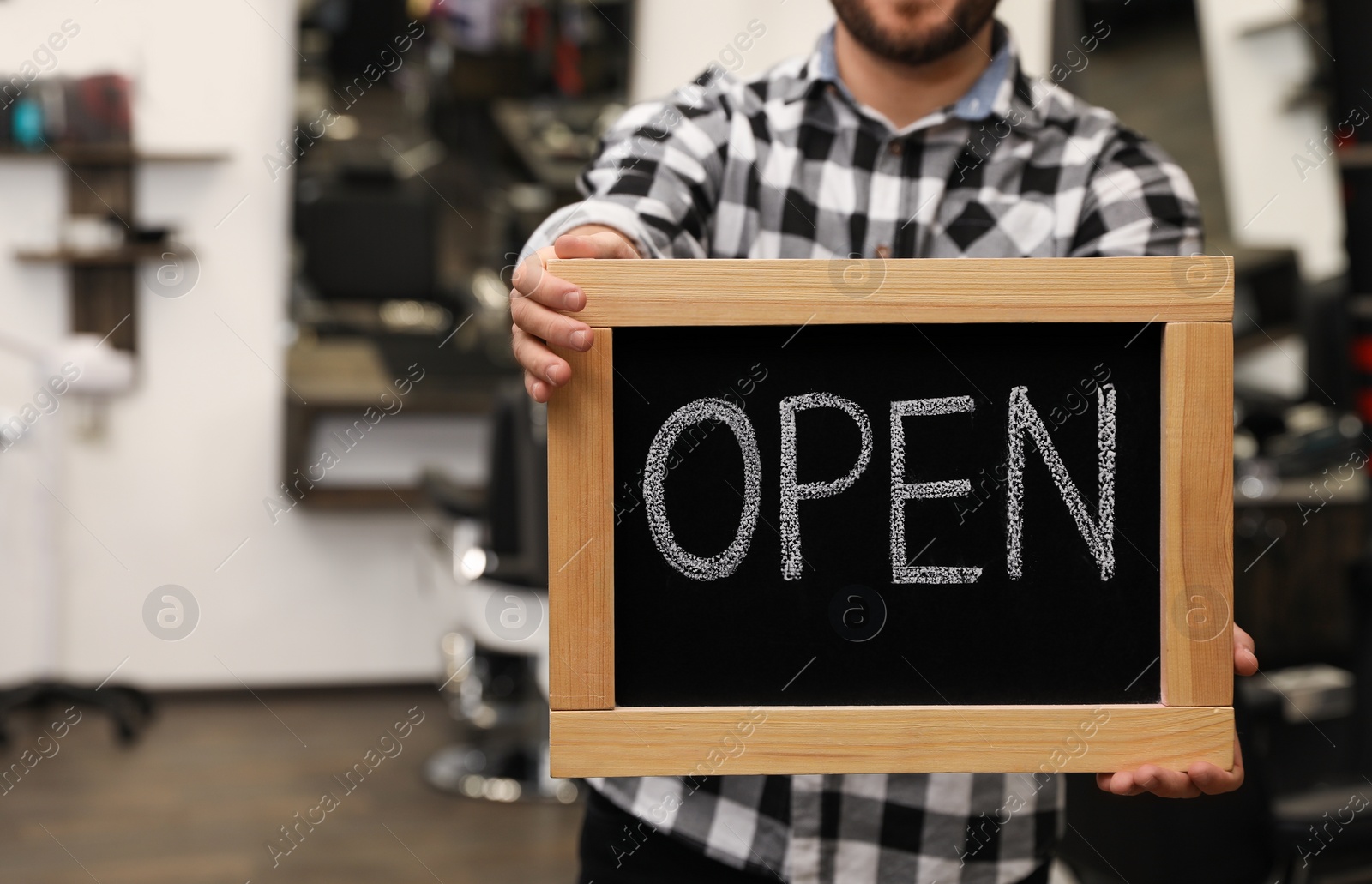 Photo of Young business owner holding OPEN sign in his barber shop, closeup