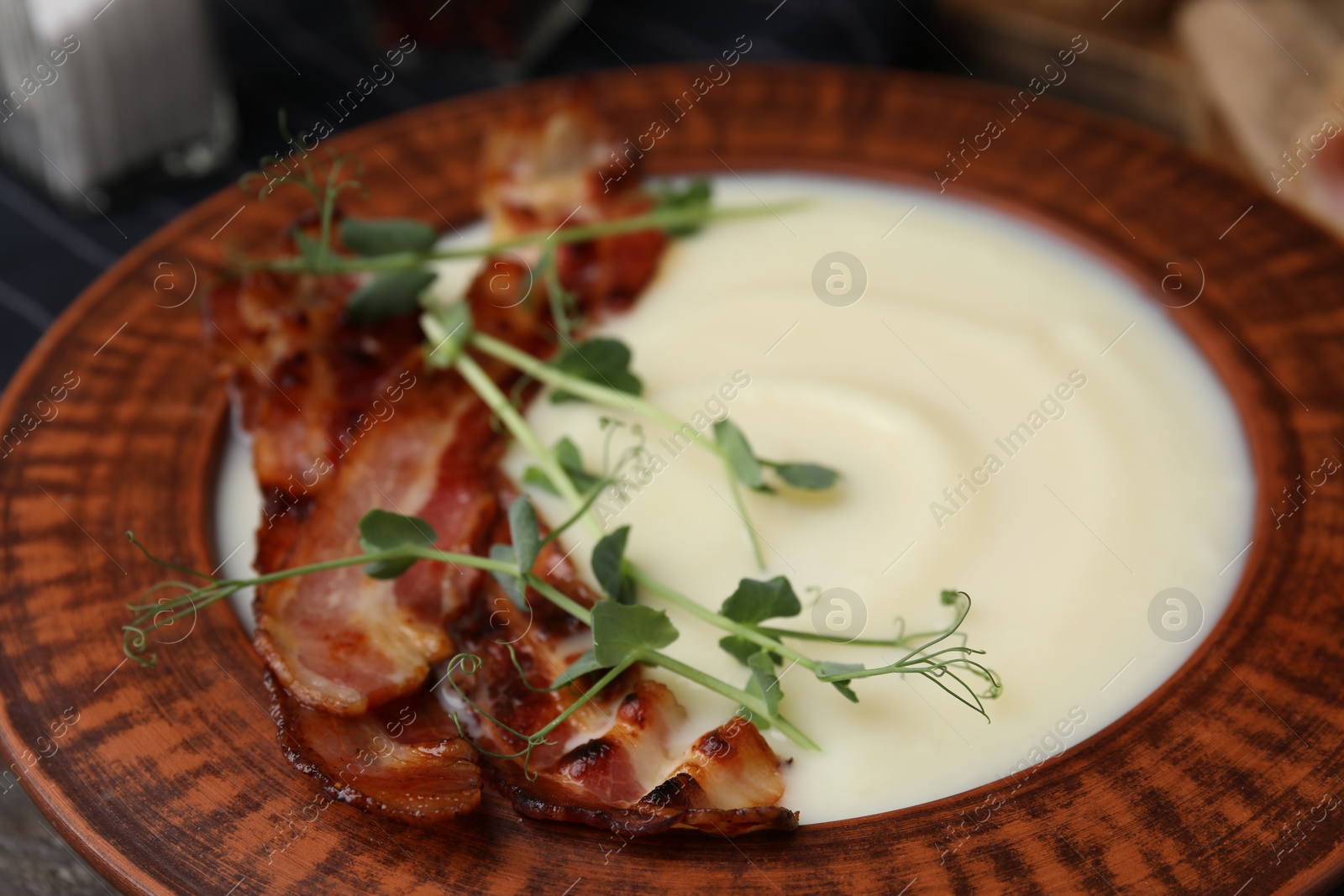 Photo of Delicious potato soup with bacon and microgreens in bowl on table, closeup