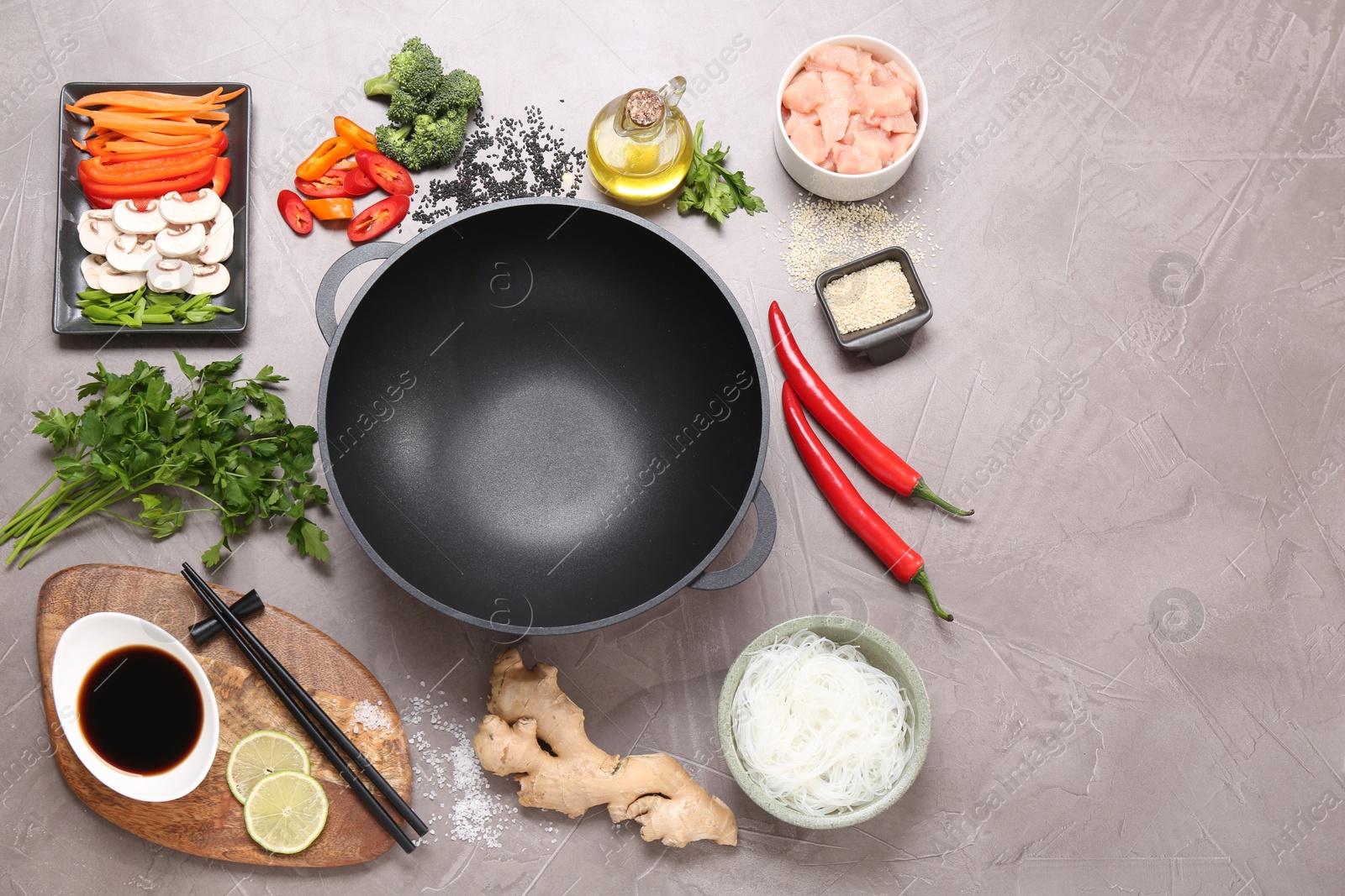 Photo of Wok, chopsticks and different products on grey textured table, flat lay. Space for text