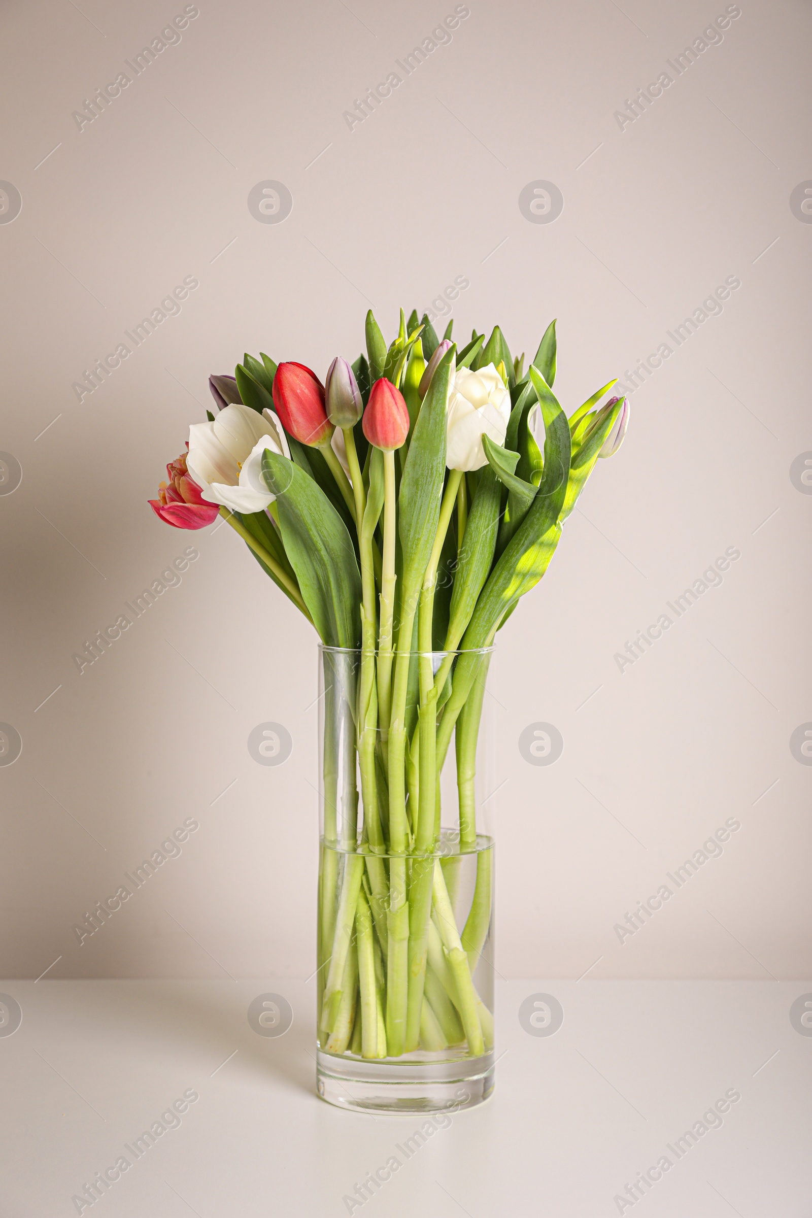 Photo of Beautiful bouquet of colorful tulips in glass vase on beige background