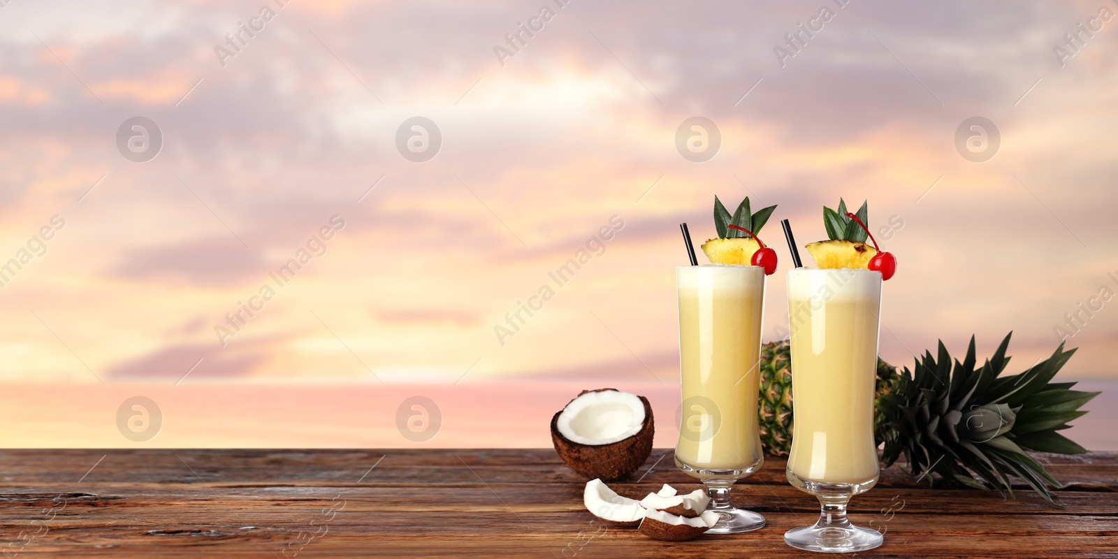 Image of Tasty Pina Colada cocktail on wooden table at sunset, space for text. Banner design