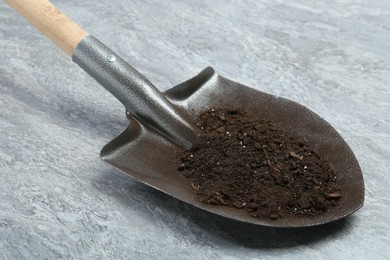 Photo of Metal shovel with fertile soil on gray textured surface