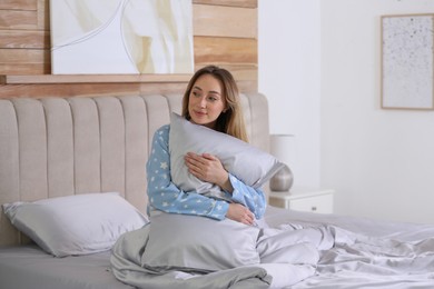 Photo of Young woman hugging pillow on comfortable bed with silky linens