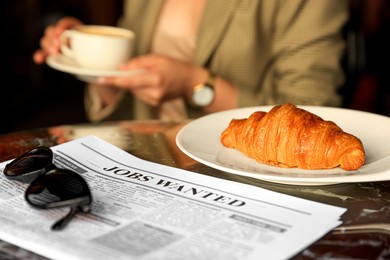 Photo of Woman sitting with cup of hot drink at table, focus on croissant