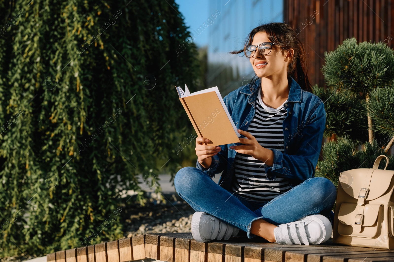 Photo of Young woman reading book on bench outdoors