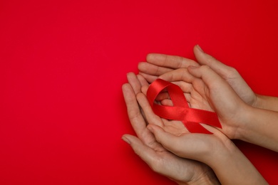 Photo of Woman and girl holding red ribbon on bright background, top view with space for text. AIDS disease awareness