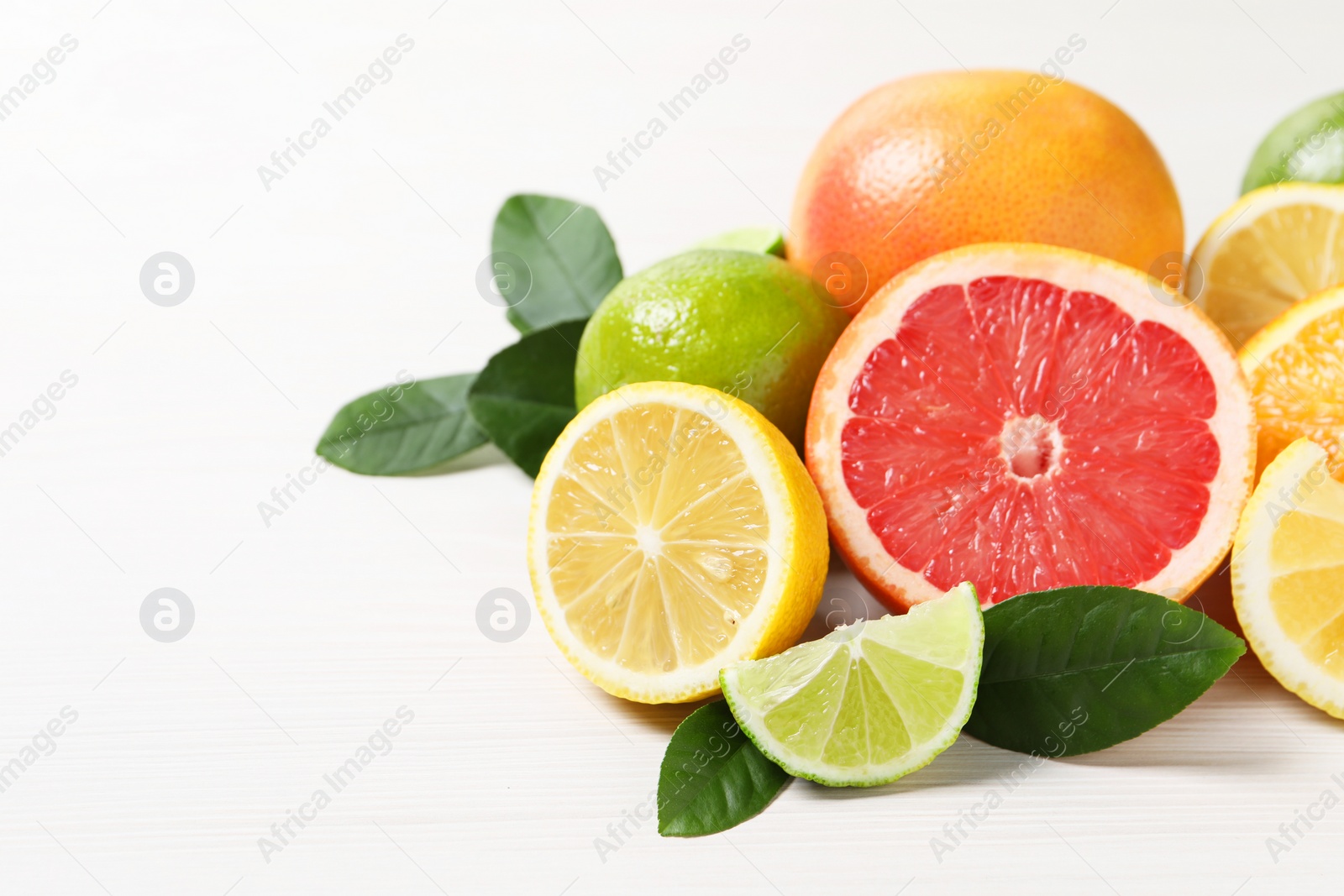 Photo of Different cut and whole citrus fruits on white wooden table, closeup. Space for text