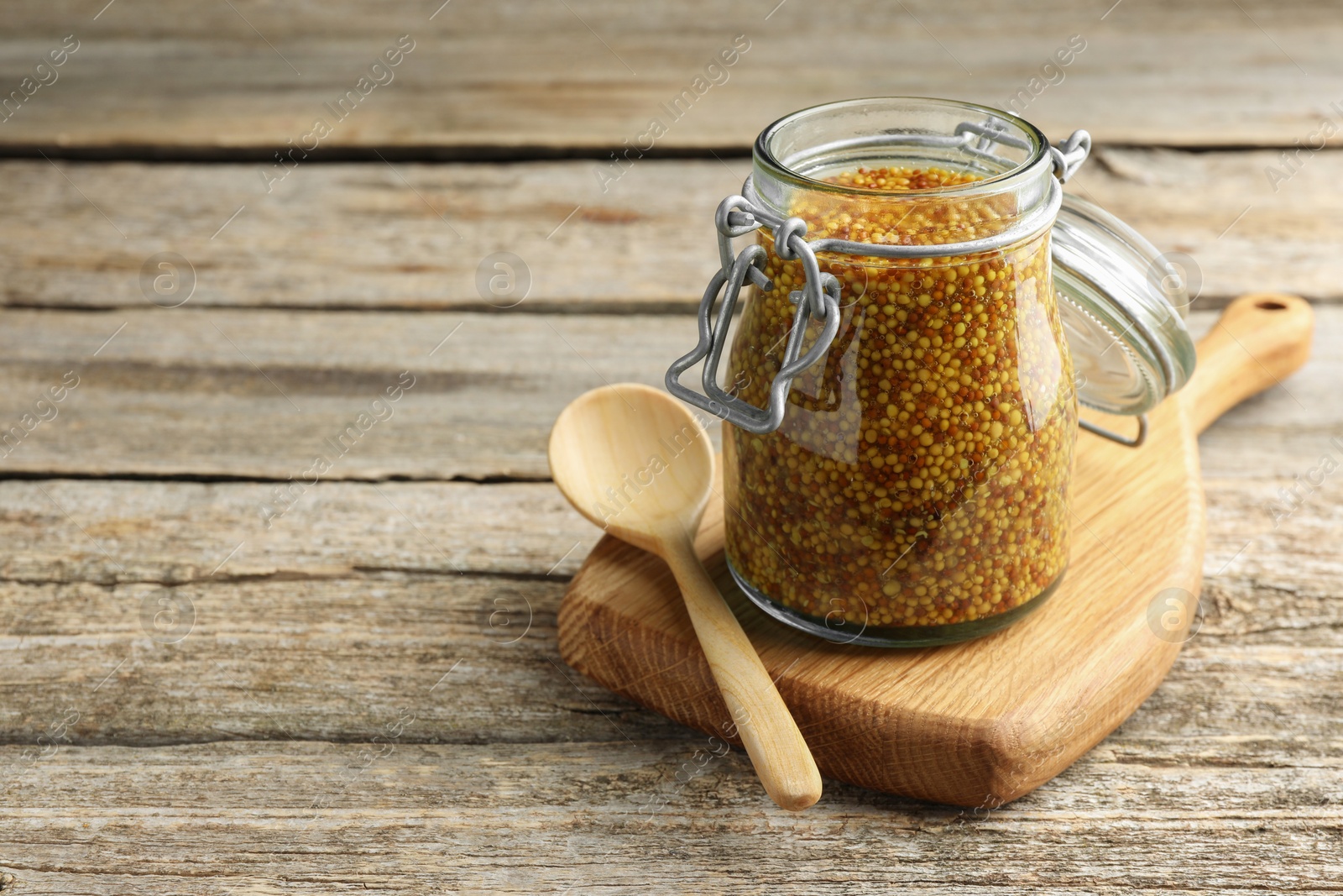 Photo of Whole grain mustard in jar and spoon on wooden table. Space for text