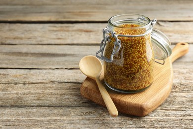 Whole grain mustard in jar and spoon on wooden table. Space for text