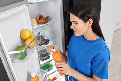 Photo of Young woman taking bottle of juice out of refrigerator indoors, above view