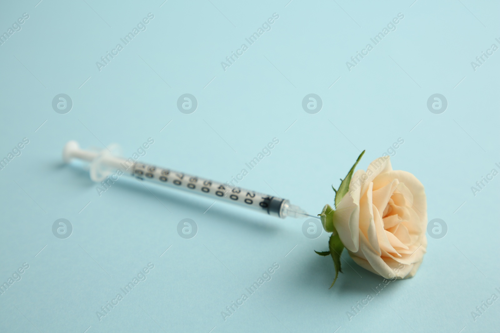 Medical syringe and beautiful rose on light blue background, closeup Photo of Medical syringe and beautiful rose on light blue background, closeup