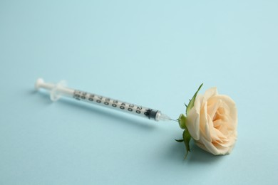Photo of Medical syringe and beautiful rose on light blue background, closeup