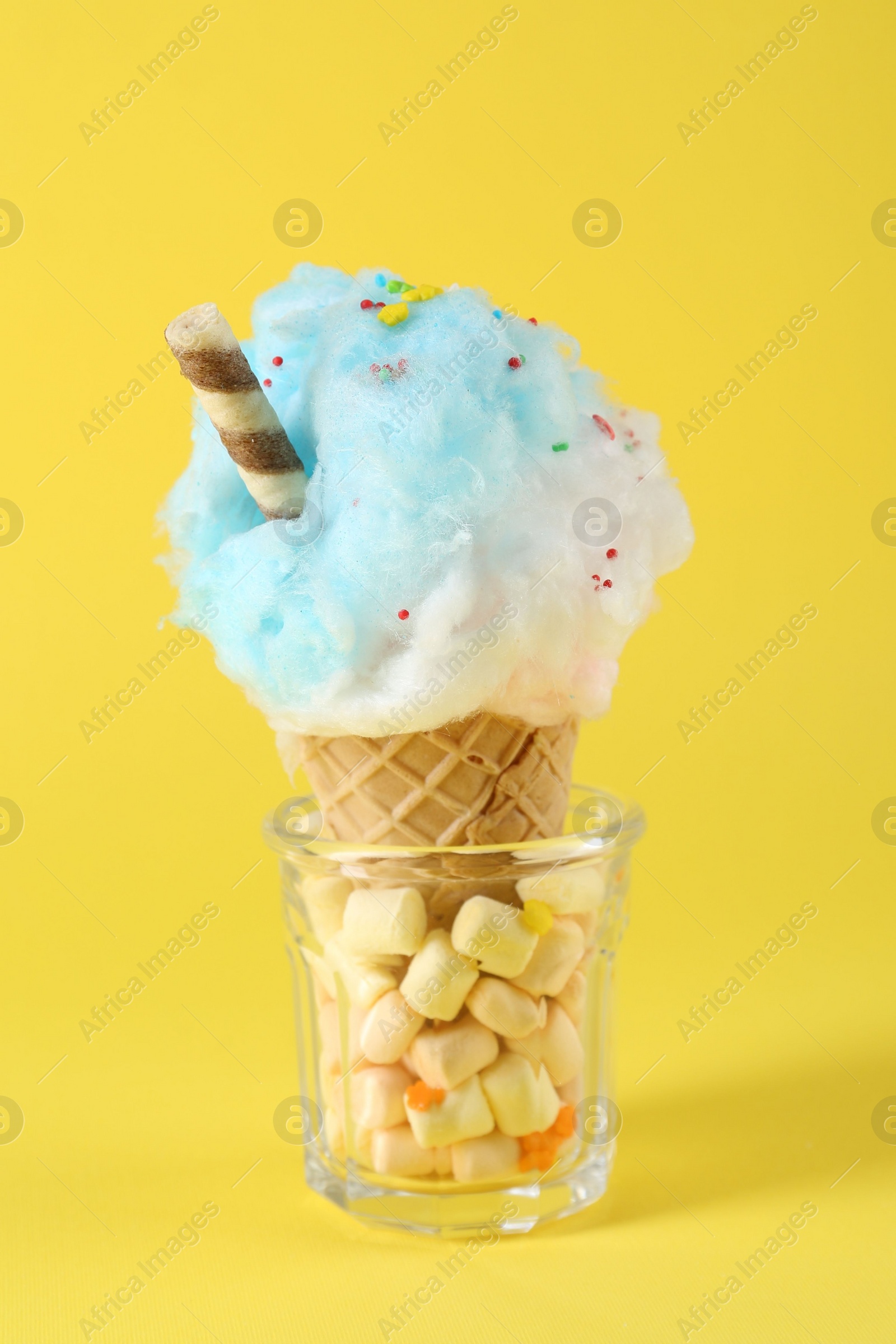 Photo of Sweet cotton candy in waffle cone on yellow background