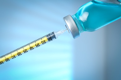 Photo of Filling syringe with medication from vial against light background, closeup. Vaccination and immunization