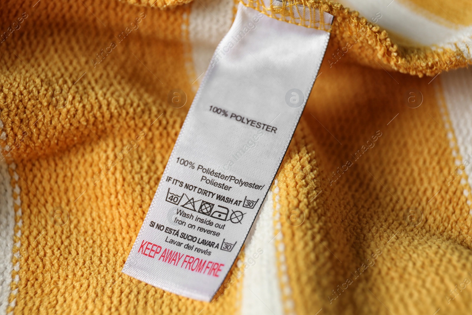 Photo of Clothing label with care symbols and material content on yellow shirt, closeup view