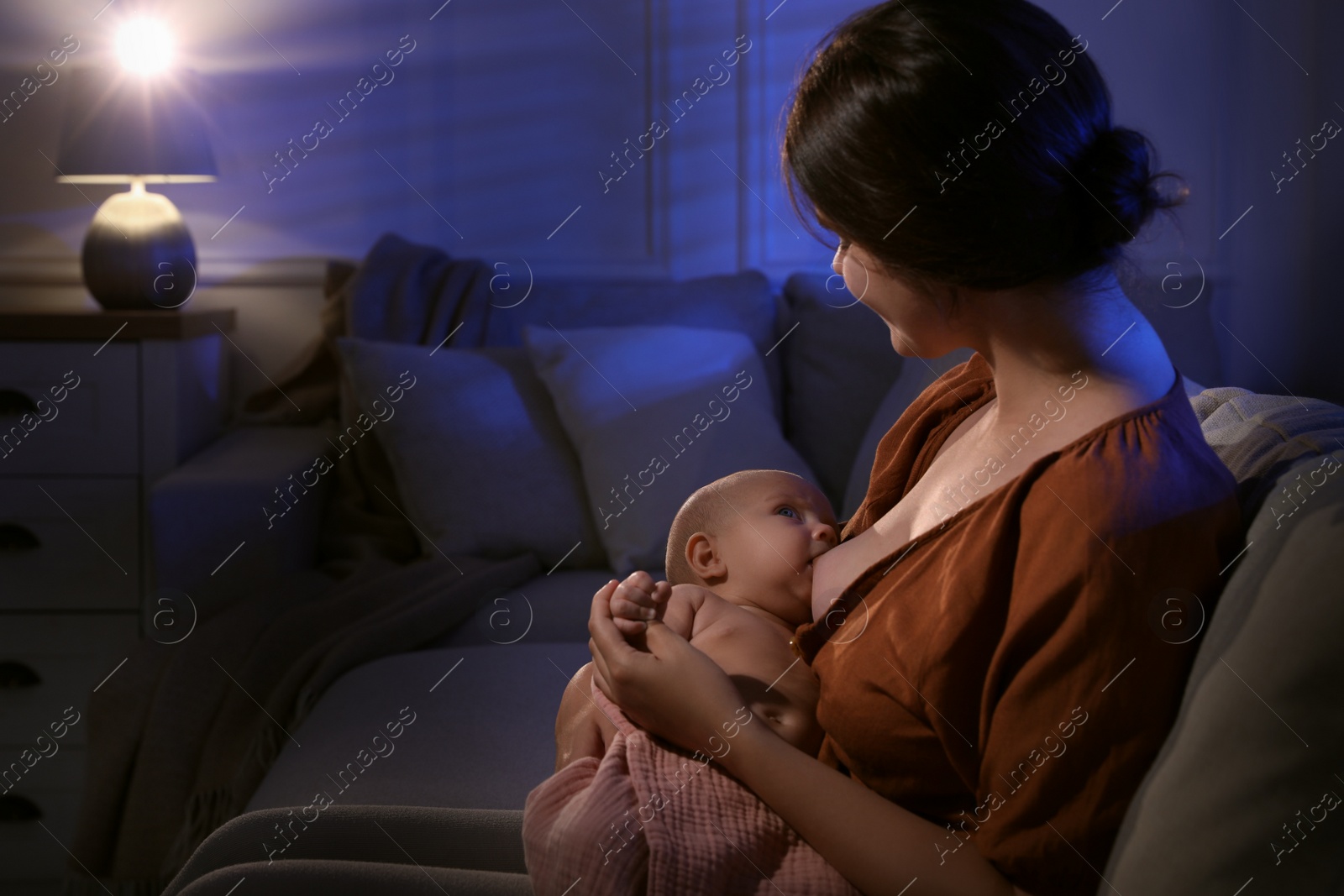 Photo of Young woman breastfeeding her little baby indoors at night, space for text