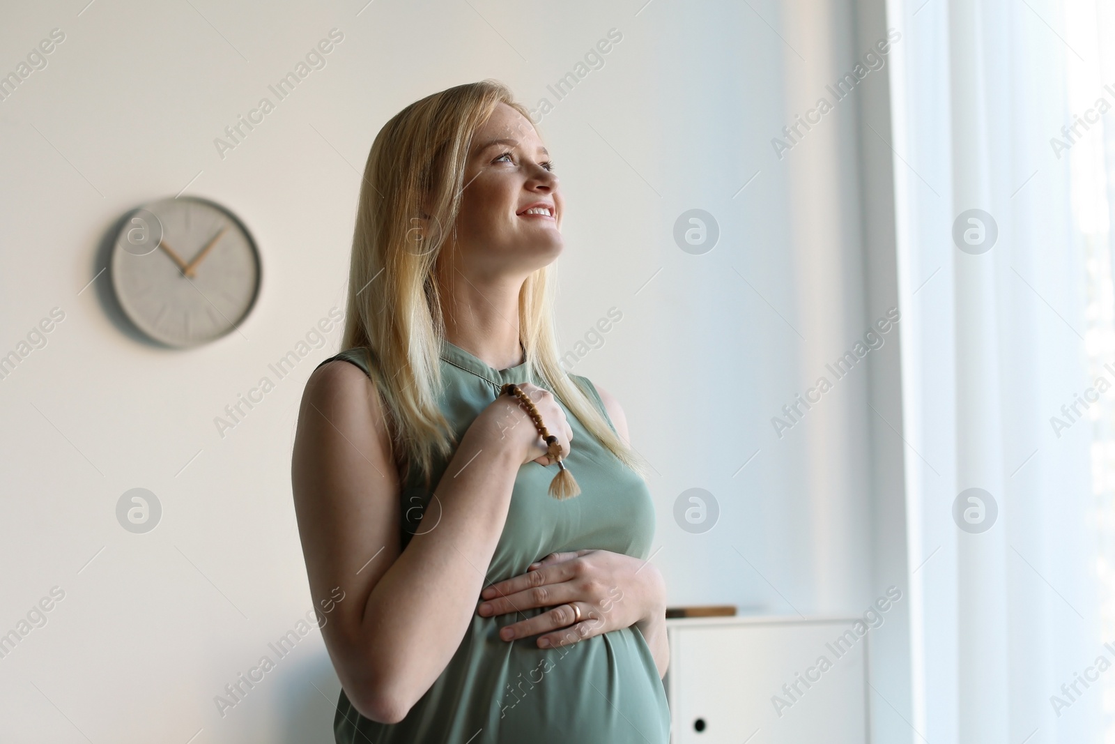 Photo of Young pregnant woman with beads praying at home. Space for text