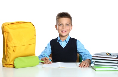 Photo of Little boy in uniform doing assignment at desk against white background. School stationery
