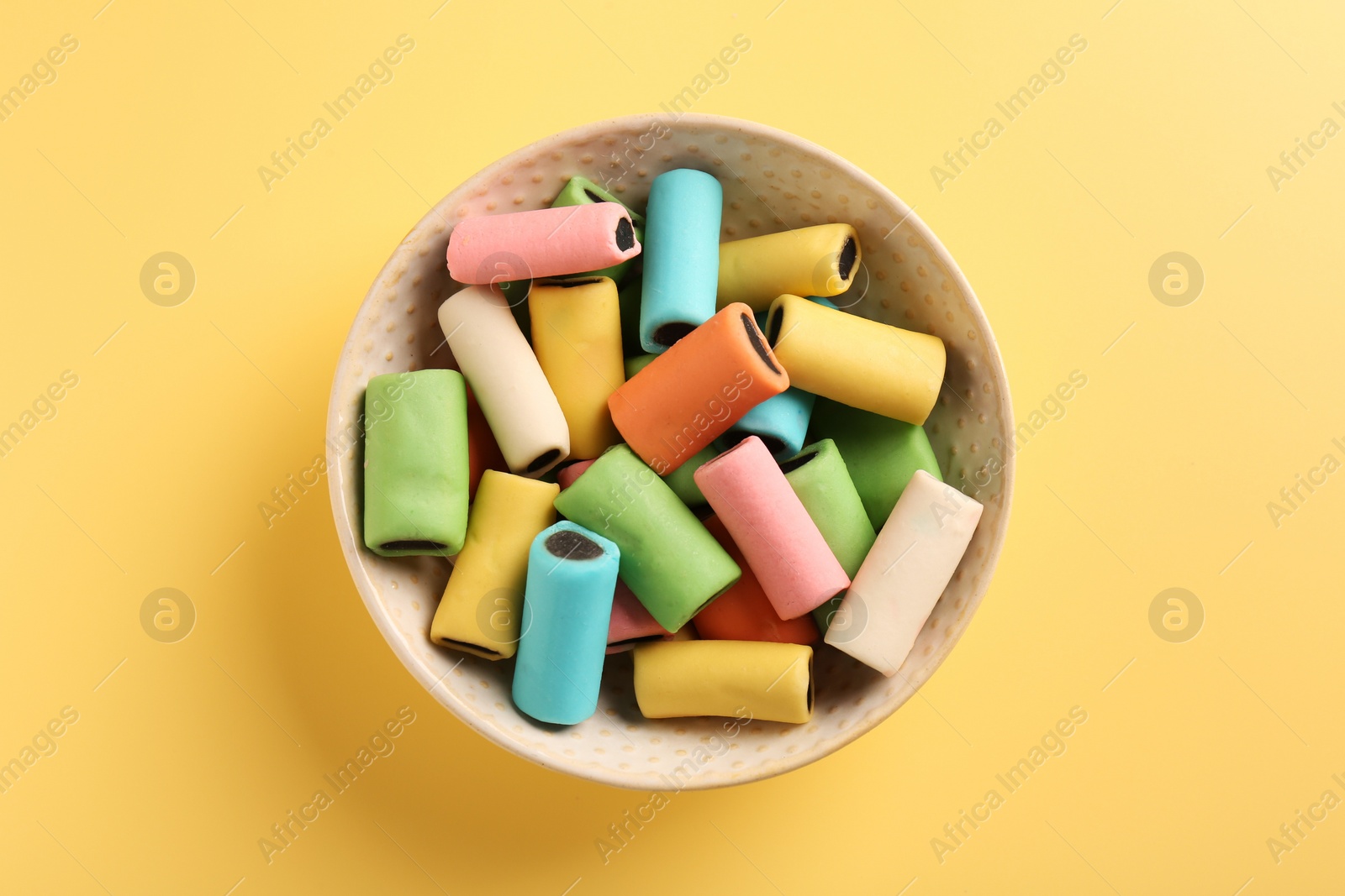 Photo of Bowl of tasty liquorice candies on yellow background, top view