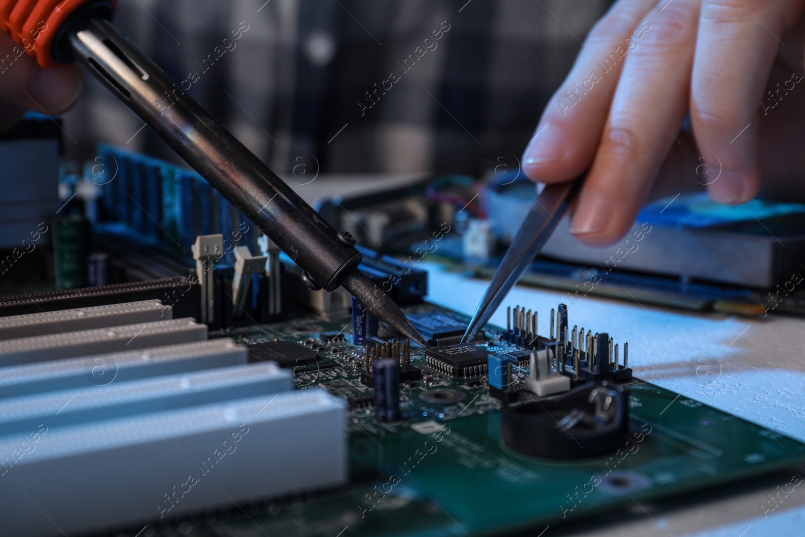 Photo of Technician repairing electronic circuit board with soldering iron at table, closeup