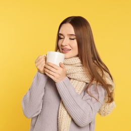 Beautiful young woman in sweater with drink on yellow background. Winter season