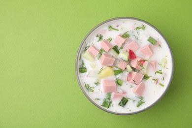 Photo of Delicious cold summer soup (okroshka) with boiled sausage in bowl on green table, top view. Space for text