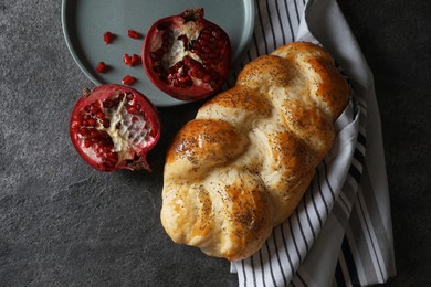 Photo of Homemade braided bread and pomegranate on grey table, flat lay. Cooking traditional Shabbat challah
