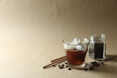 Photo of Refreshing iced coffee in glass, beans and straws on beige background. Space for text